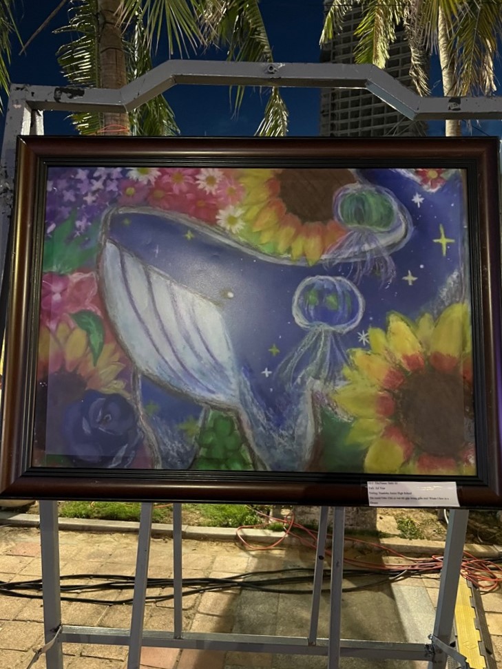 ダナン市日越フェスティバル会場の公園で絵画が展示されています。絵にはクジラが大きく描かれており、その周りに様々な花やくらげが描かれています。
