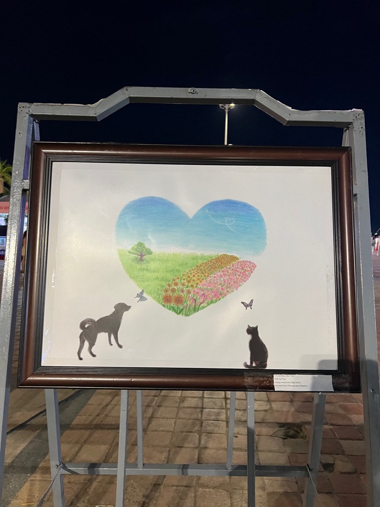 ダナン市日越フェスティバル会場の公園で絵画が展示されています。絵の中心にはハートがありその中に草原と花畑が描かれています。ハートの周りには犬、猫、蝶が描かれています。