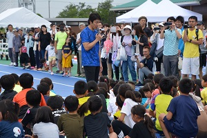 競技場で、朝原選手がたくさんの子供達の前で話をしている、かけっこ教室の様子の写真