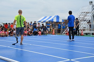 保護者や子供達が並んで座っている前で、朝原選手と山本選手が話をしている、かけっこ教室の写真