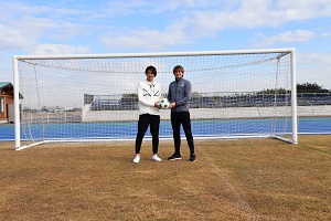 青空の下、サッカーゴールの中央に立つ、吉田眞紀人選手とカレン・ロバート選手がサッカーボールを2人で持っている写真