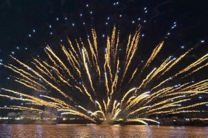 金色の水上花火が大きく広がり、水面に光が反射する風景の写真