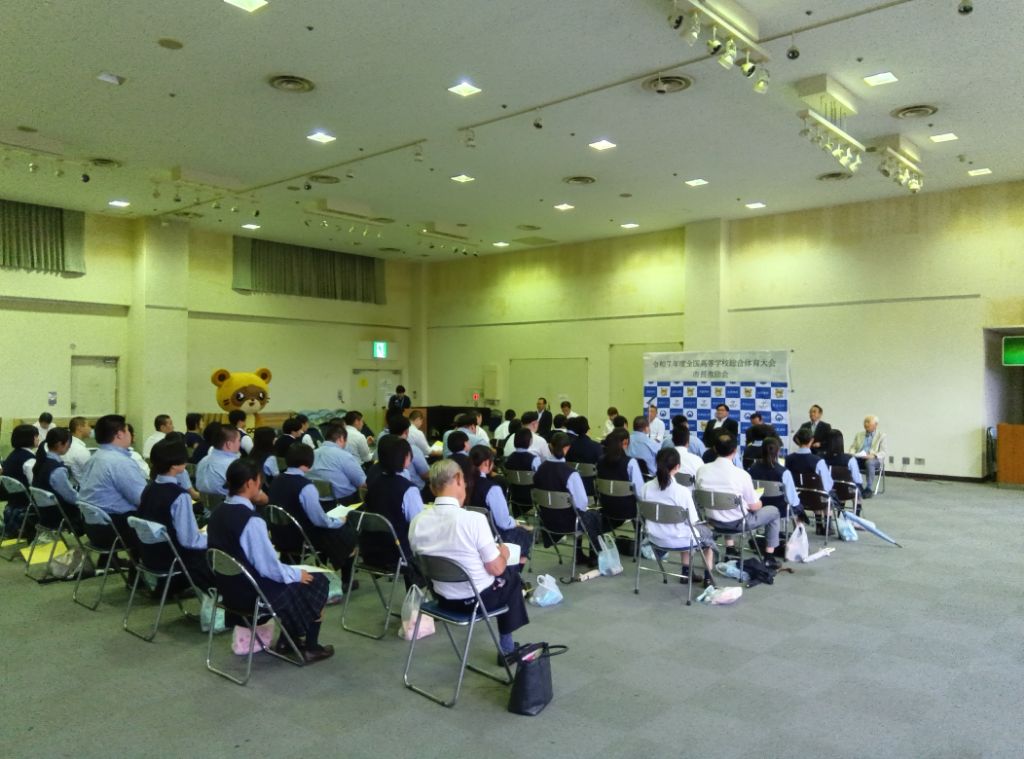 ホールの中で学生たちがパイプ椅子に座っている激励会中の写真