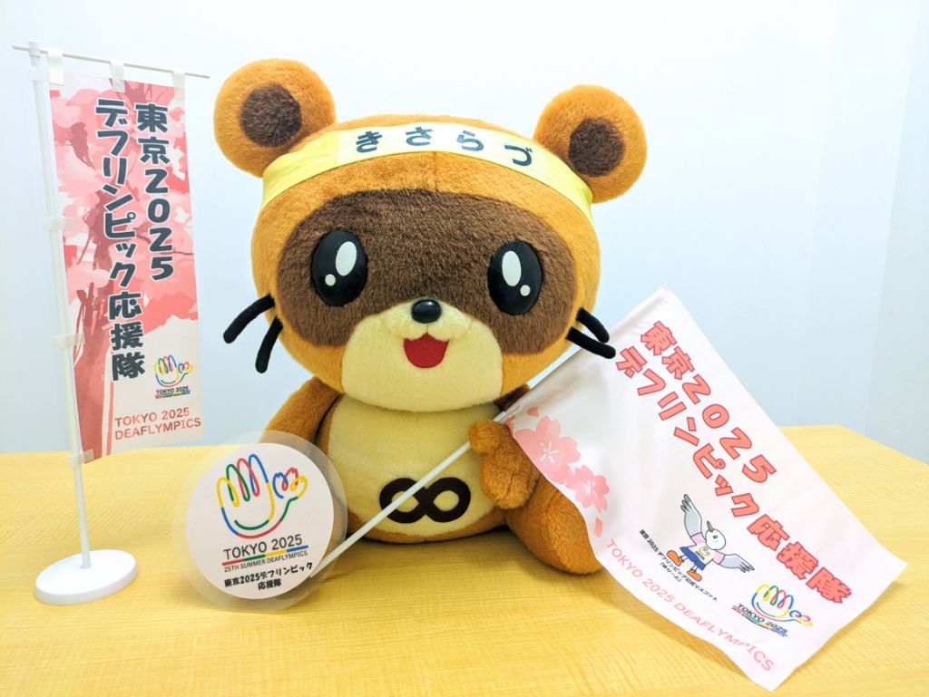 木更津市マスコットキャラクターきさポンが東京2025デフリンピック応援隊の旗などを持っている様子