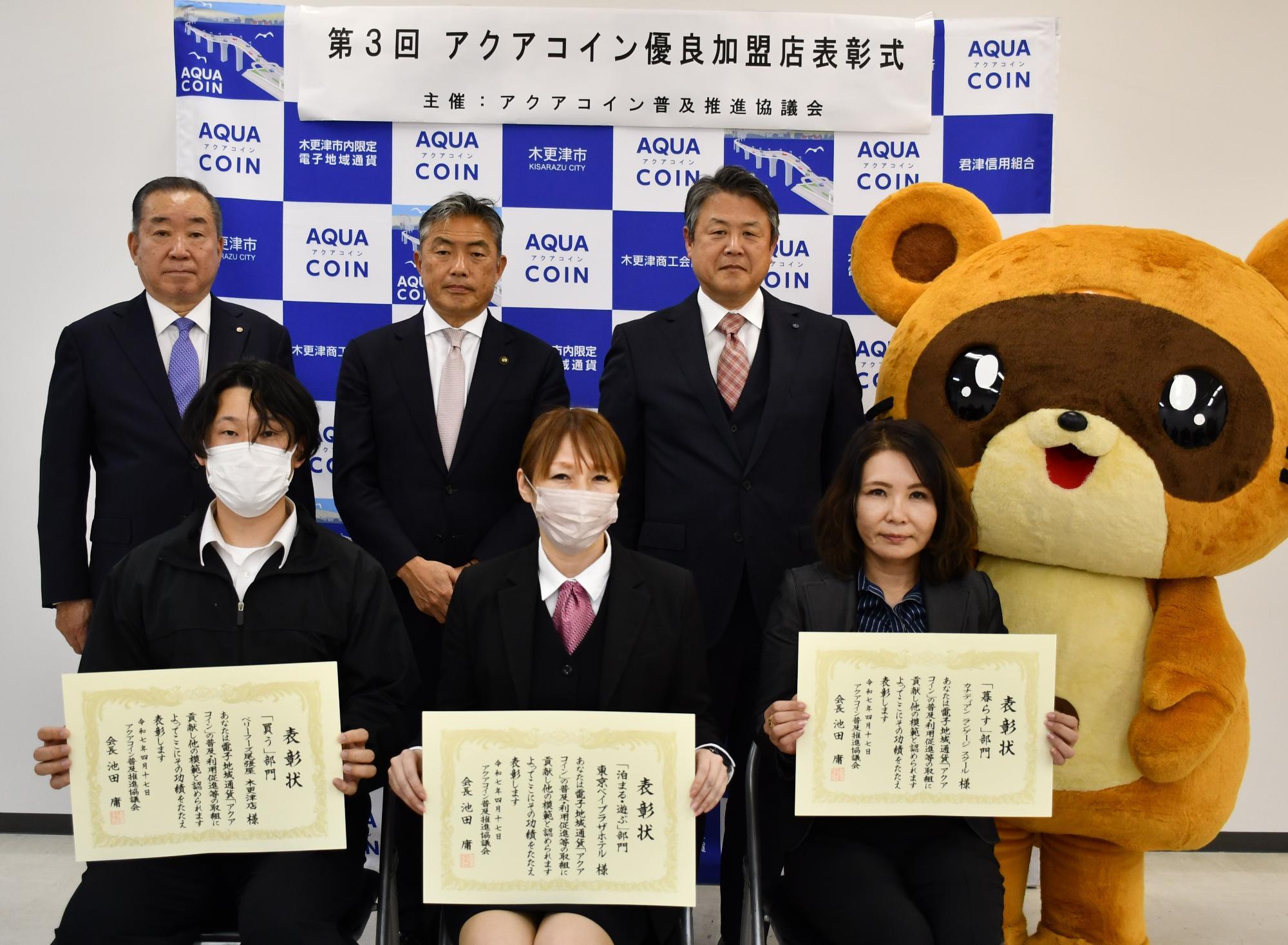 後列に3人前列に3人座ってきさポンが横に立っている記念写真の様子