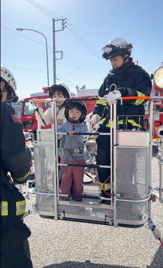 女の子と男の子が消防士と一緒に消防はしご車へ乗っている