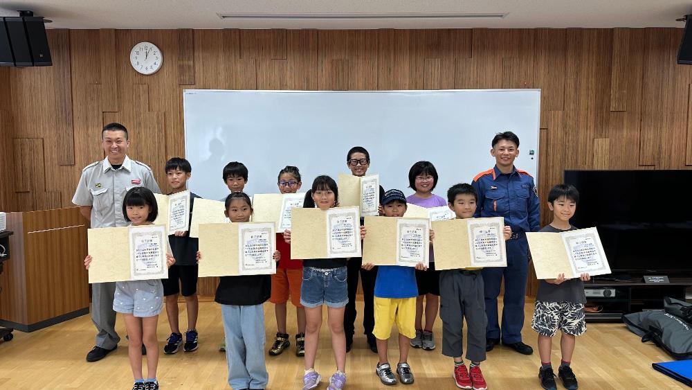 両端に消防職員が立ち、前後2列に並んだ11名の子どもたちが終了証を手にした集合写真