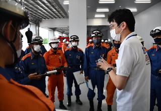 白シャツを着た男性講師の周りに活動服を着用した隊員の方々が集まり、資機材の取り扱いの説明を受けている様子の写真