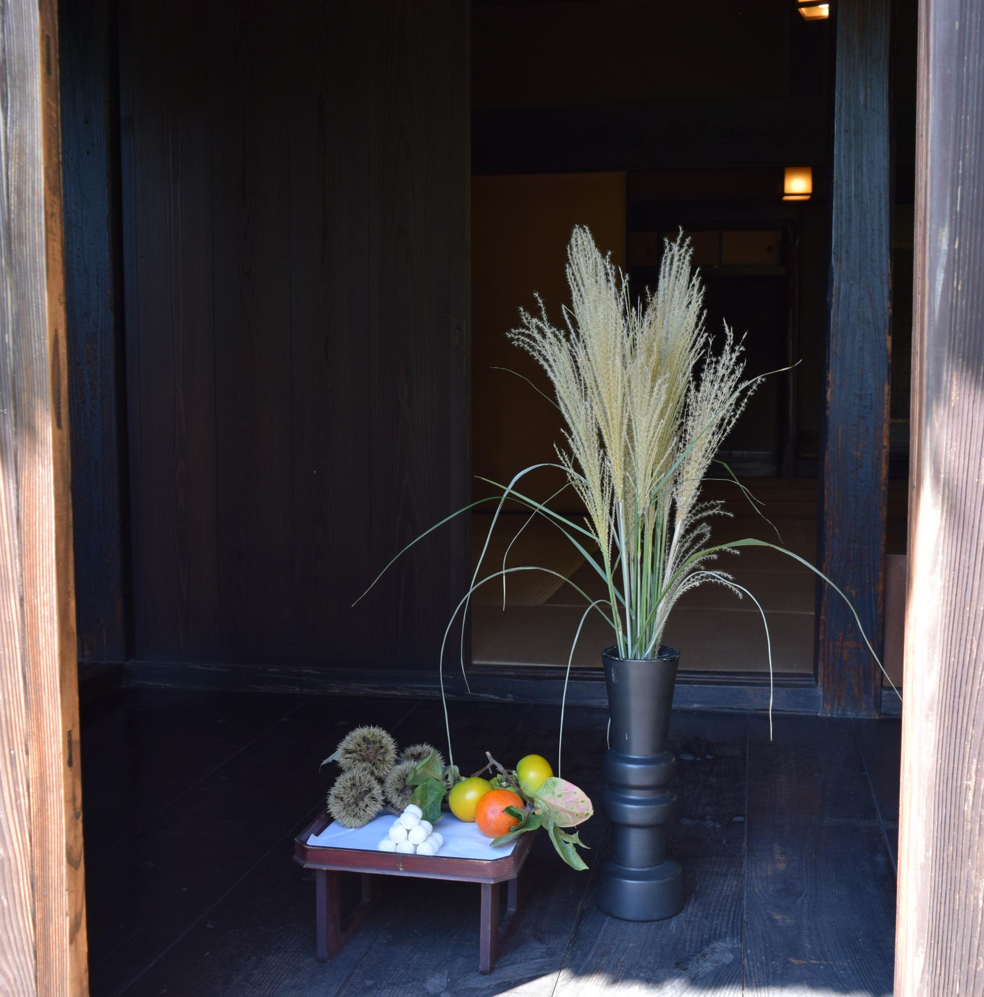 木造家屋の旧安西家住宅に、ススキ、団子、栗、柿が十五夜の飾りつけとして展示されている写真