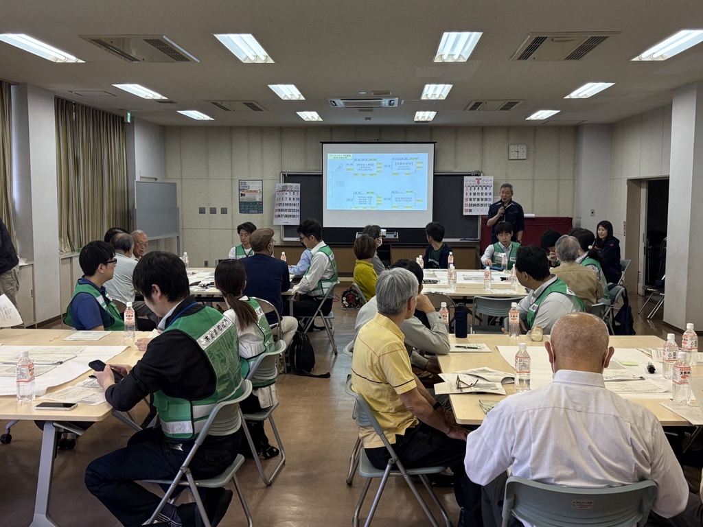市の職員とまちづくり協議会のみなさんが清見台公民館の集会室に集まり、訓練説明を聞く様子