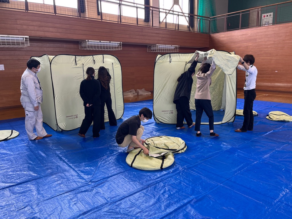 市の職員が3人一組で避難所用の間仕切りテントを組み立てている様子