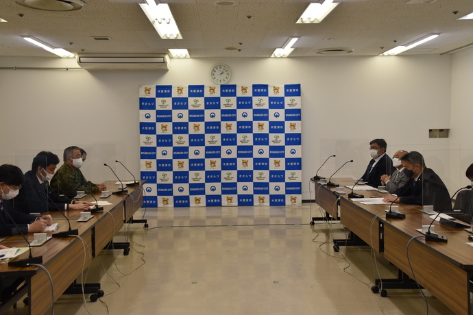 木更津市のバックボードが置かれた室内の左右に、アクリル板で仕切られた長机が設置され、岸防衛大臣や渡辺市長、重城市議会議長、関係者が座り、面会している様子の写真