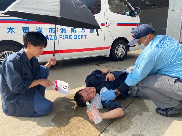 救急車の前で倒れる傷病者に、手当をする男性2名を描き、熱中症を注意喚起する画像