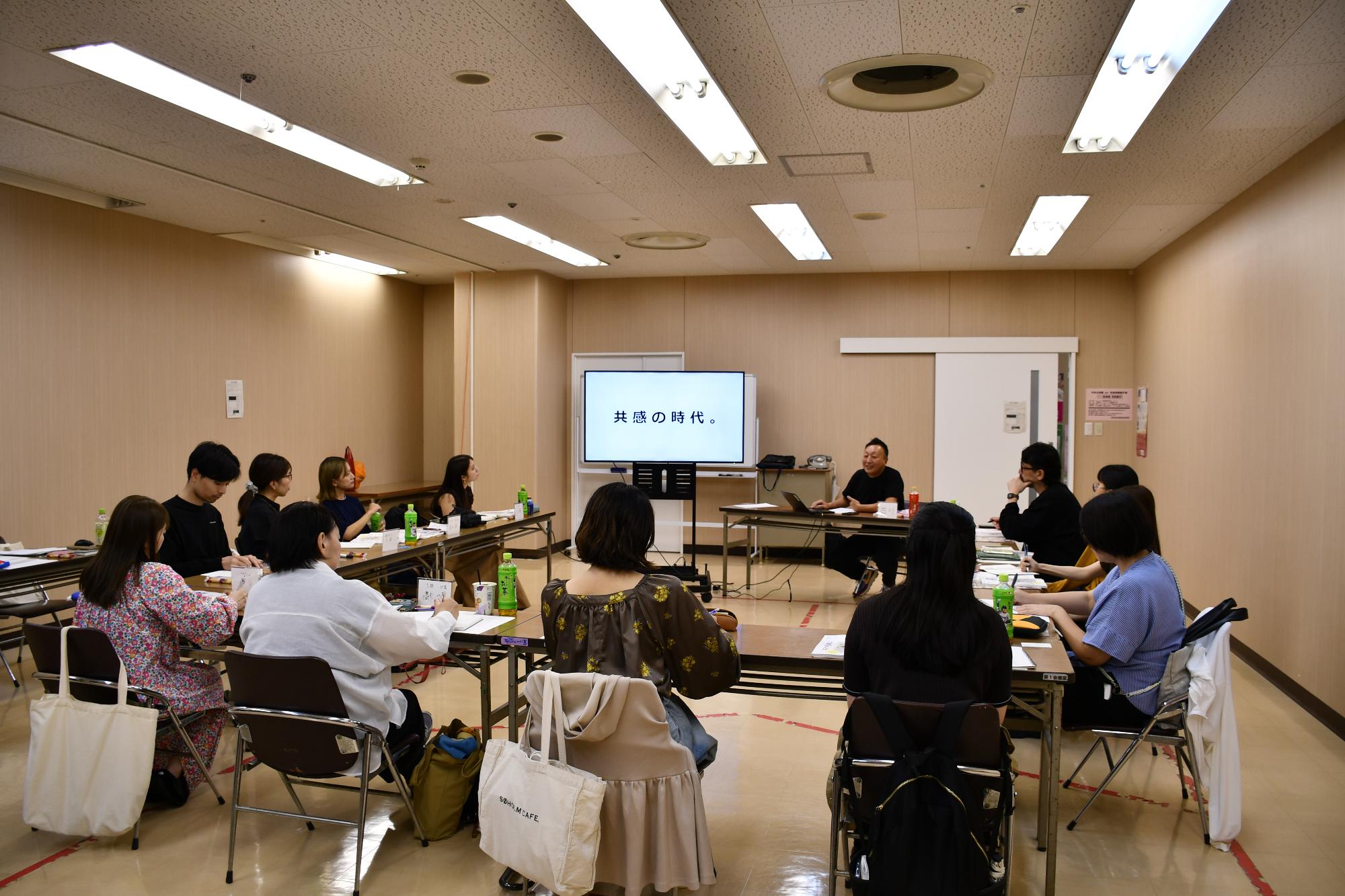 会議室の中で市民ライター11名がコの字型に座っており、講師が部屋の一番前で話をしている様子