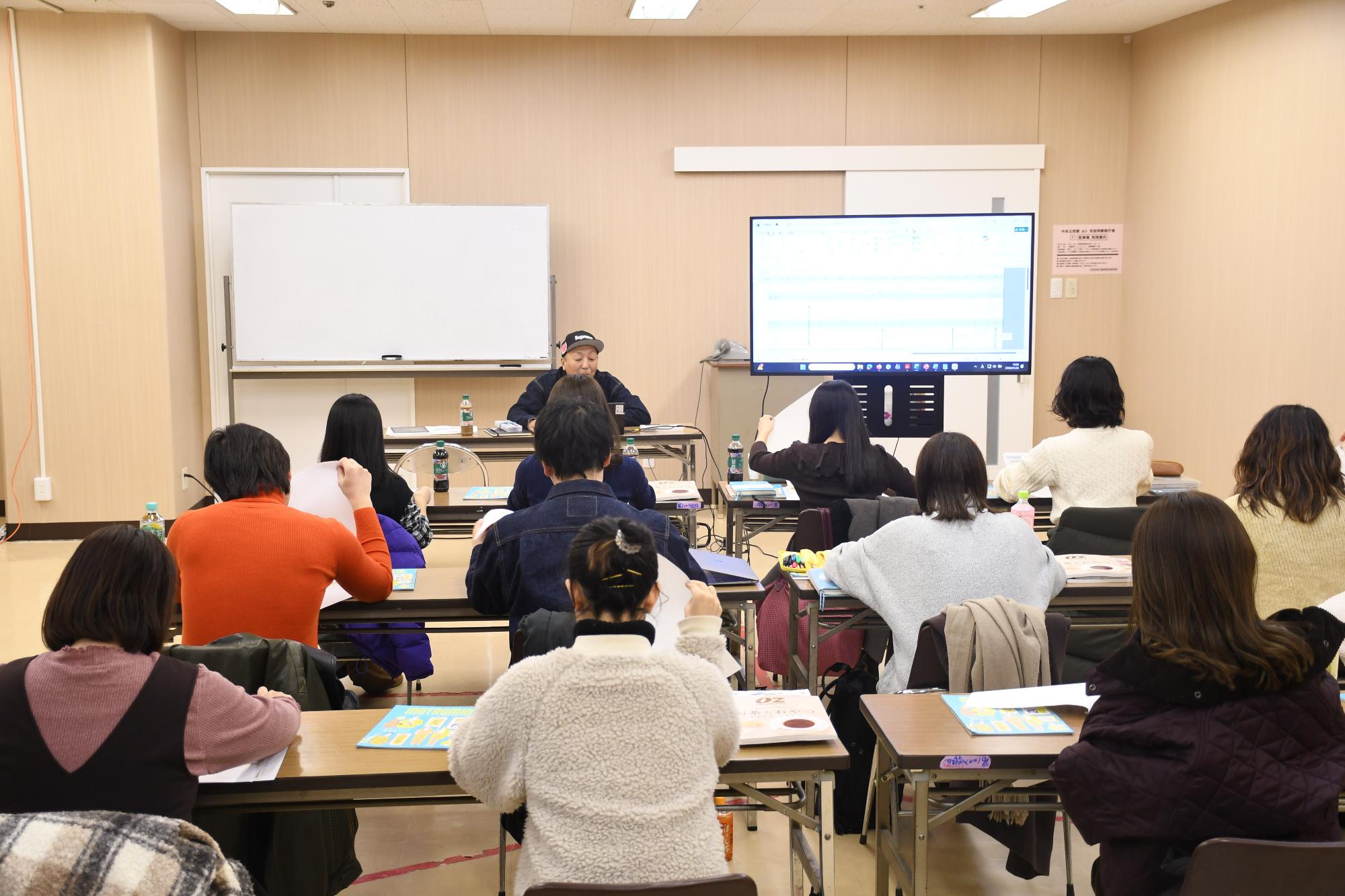 前で講師が話をしているのを市民ライターが聞いている様子