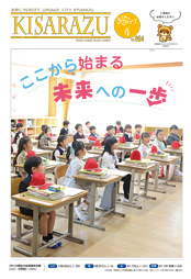 広報きさらづ4月号表紙。「ここから始まる 未来への一歩」という文字と、市内小学校の教室で、小学1年生が座席に座っている様子の一枚絵の写真。机の上には赤白帽子や教材が置かれている。