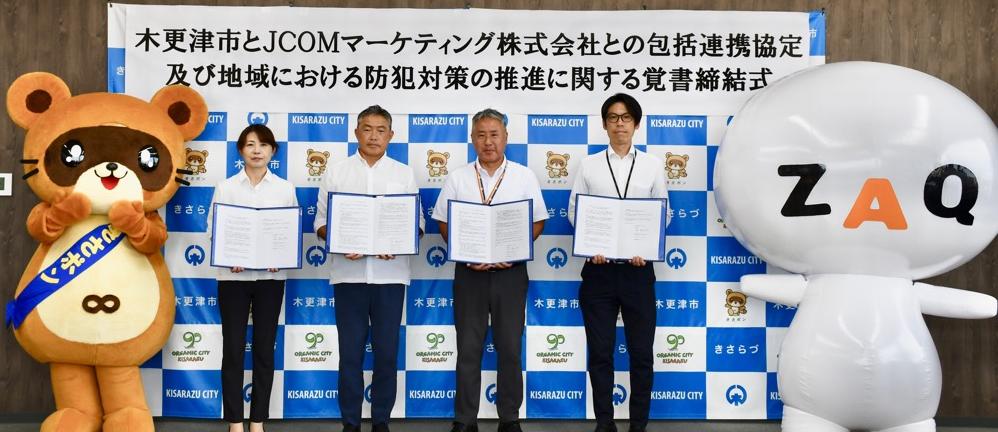 左から、木更津市マスコットキャラクターきさポン、協定書および覚書を手に持つ木更津市副市長、木更津市長、JCOMマーケティング株式会社木更津オフィス越路局長、同じくグループマネージャー藤井様、JCOMキャラクターざっくぅ