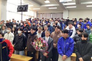 講演後にいただいた花束をもつ渡辺市長と学生の集合写真