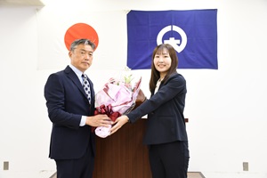 演台の前で渡辺市長が女性からピンク色の紙で包まれた花束を受け取っている花束贈呈の記念写真