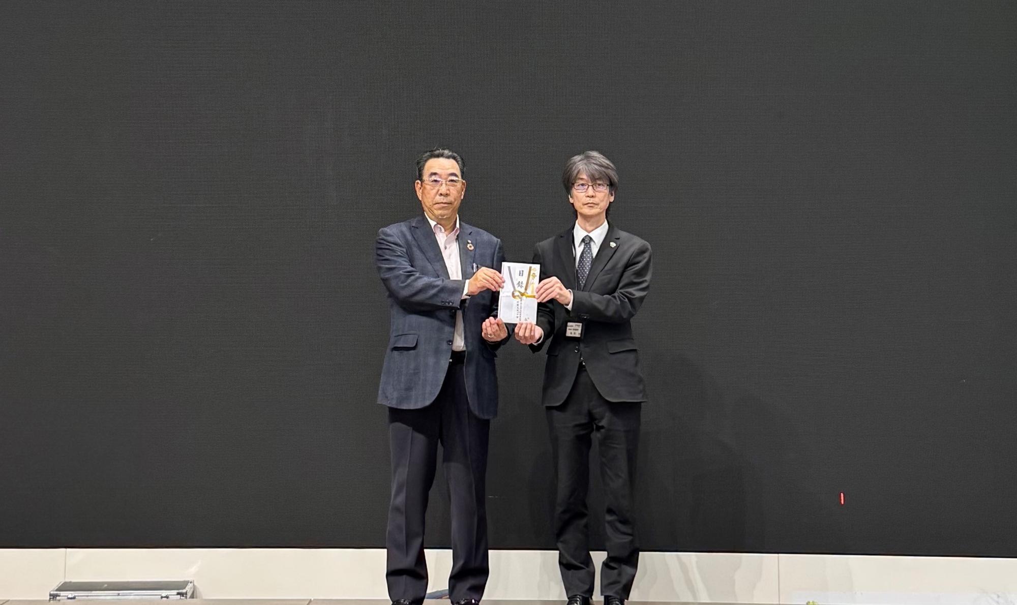 横断旗寄贈の写真(左側に、AD千葉支店プロ会 石井様、右側に、木更津市 亀田教育部次長)