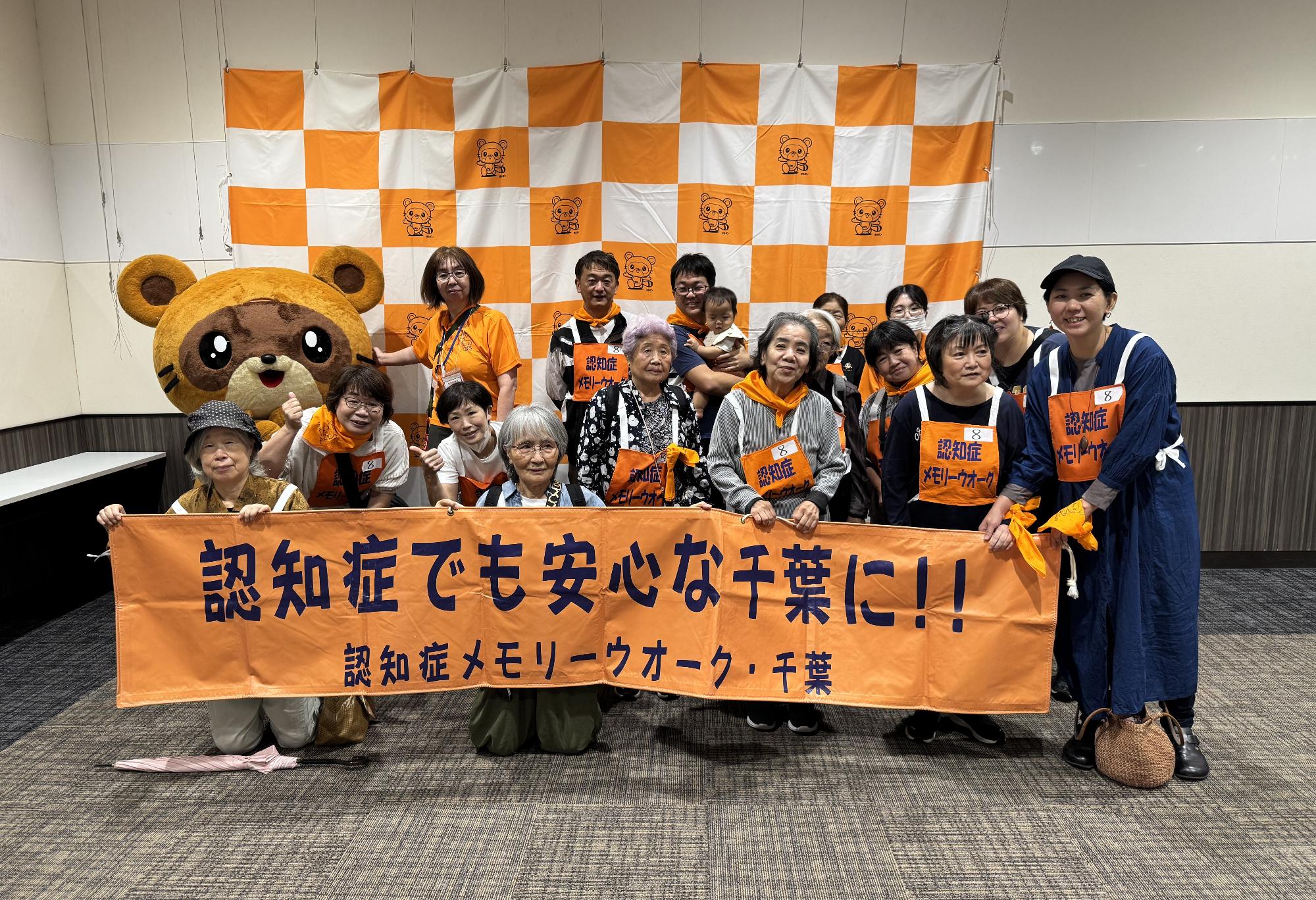 メモリーウオークスタート前に参加者が認知症普及啓発の横断幕を提示しながら木更津市のマスコットキャラクターのきさポンと一緒に記念撮影をしている様子