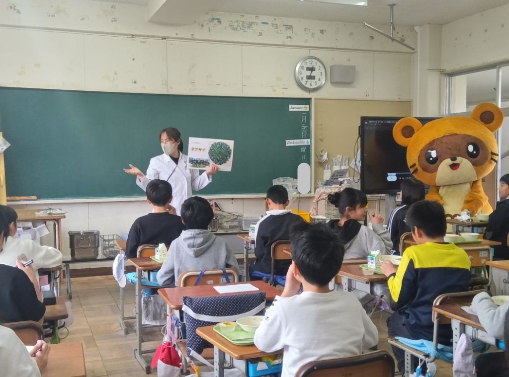 タアサイの写真を持った栄養士が子供たちに説明をしている写真