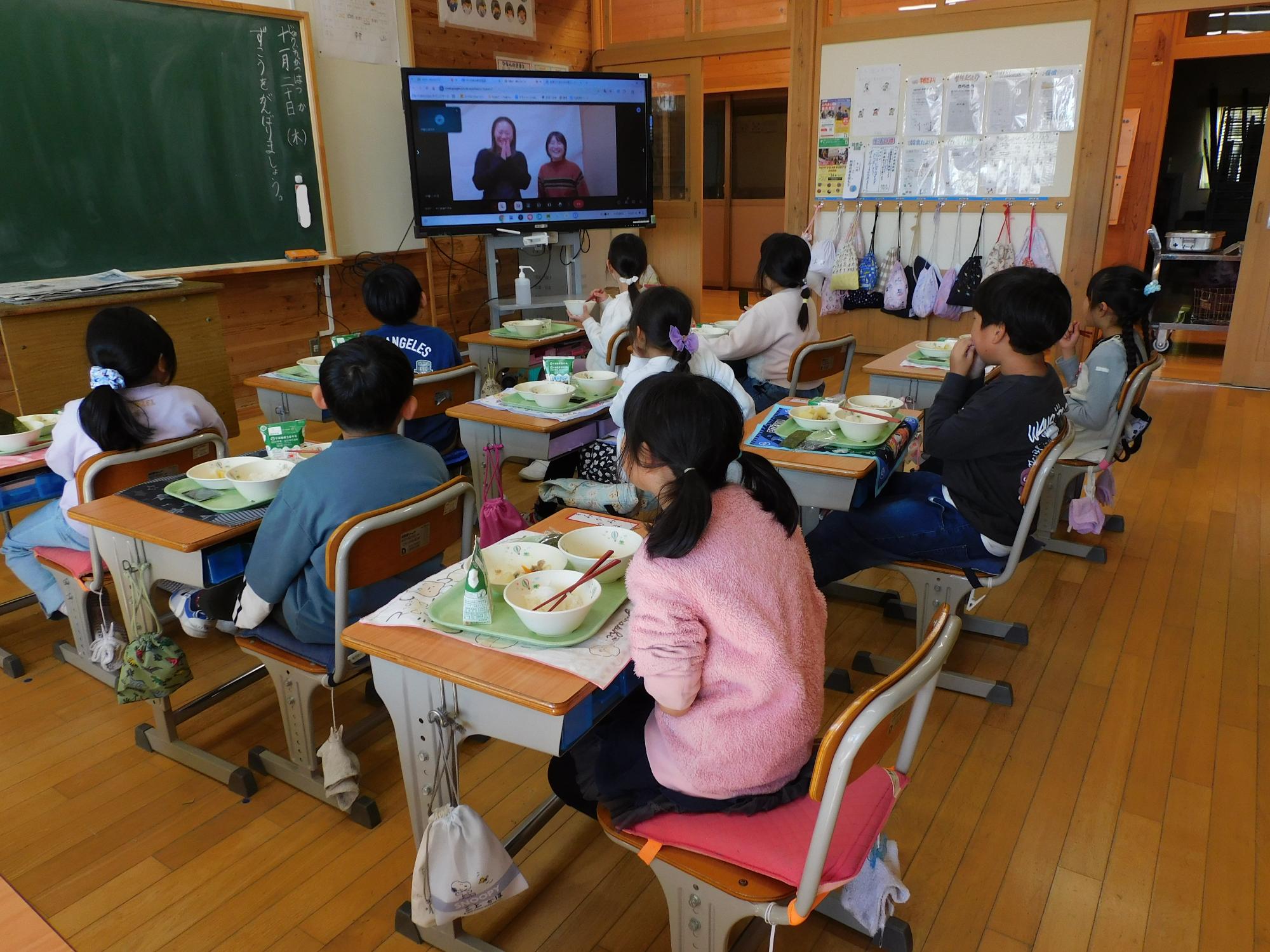 給食を食べながら、テレビ放送で生産者の話を聞く児童