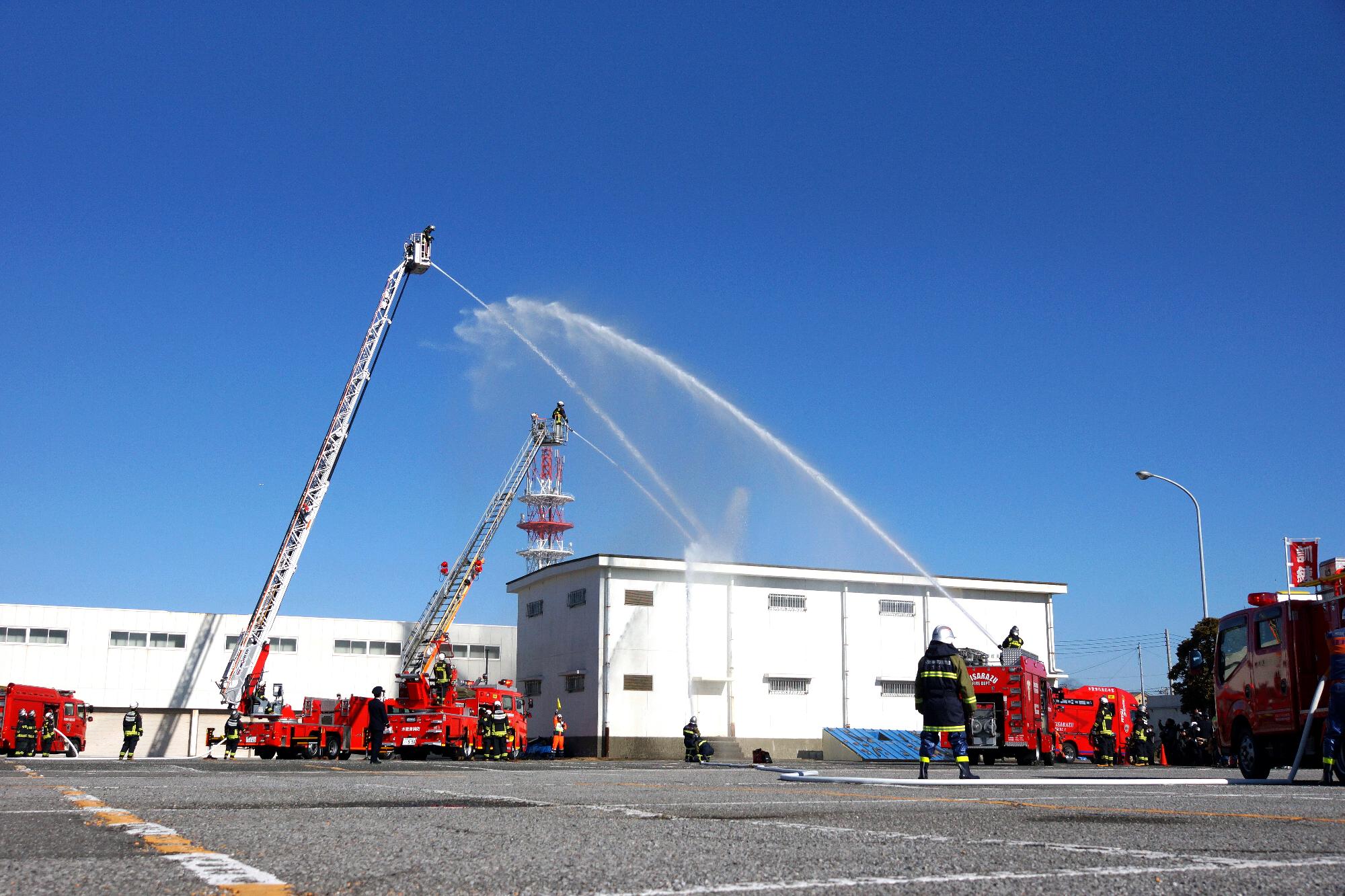 消防車1台が地上から、はしご車2台が約10メートルほどの高さから一か所へ向けて一斉に放水している様子
