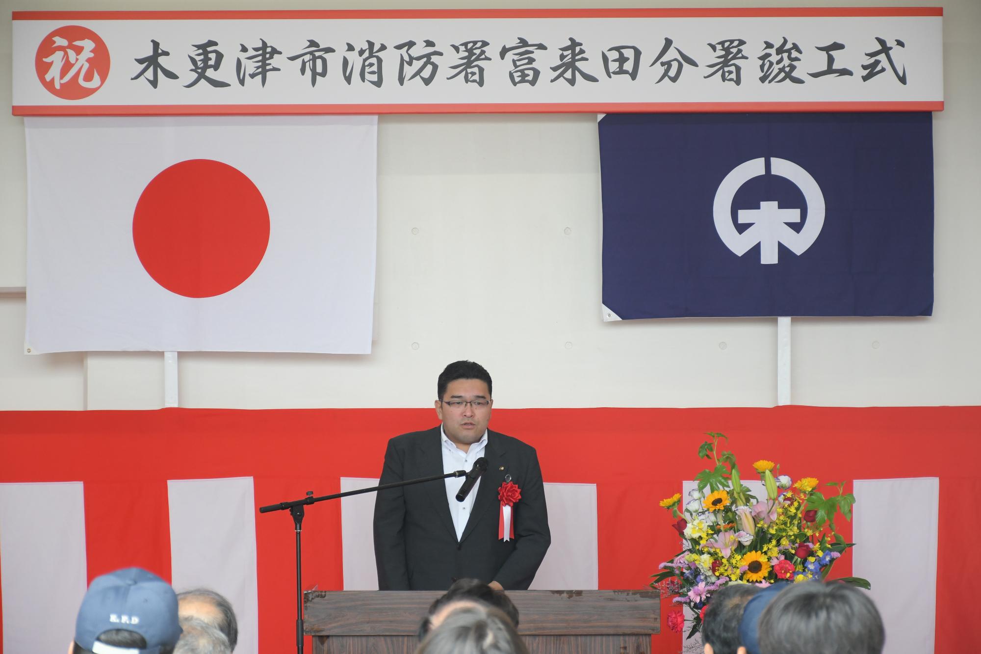 草刈市議会議長が、木更津市消防署富来田分署竣工式の場で、壇上に上がり祝辞を述べている写真。