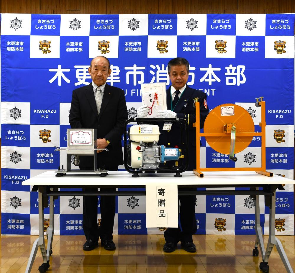 松本副会長と石井消防長がホース洗浄機の後ろに立っている