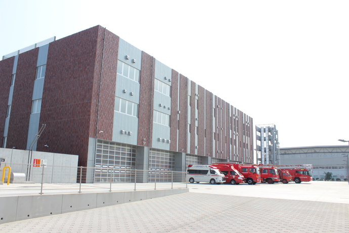 レンガ調とグレー色の壁で3階建ての建物の前に4台の消防車と1台の救急車が駐車している消防署本署の施設外観の写真