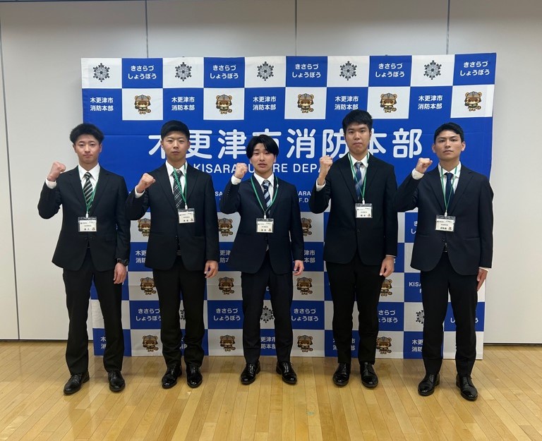 スーツ姿の5名の新規採用職員が、並んでガッツポーズをしている集合写真