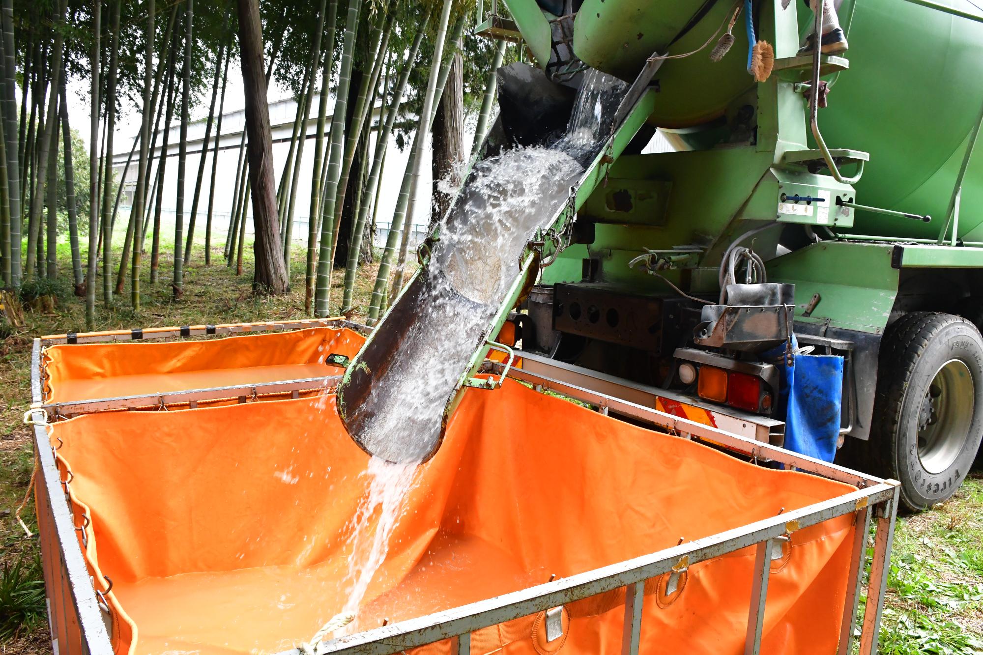 青空の下、消防職団員にて設置した水嚢に、消防用水を運搬している生コンクリートミキサー車から水嚢に消防用水を供給している様子