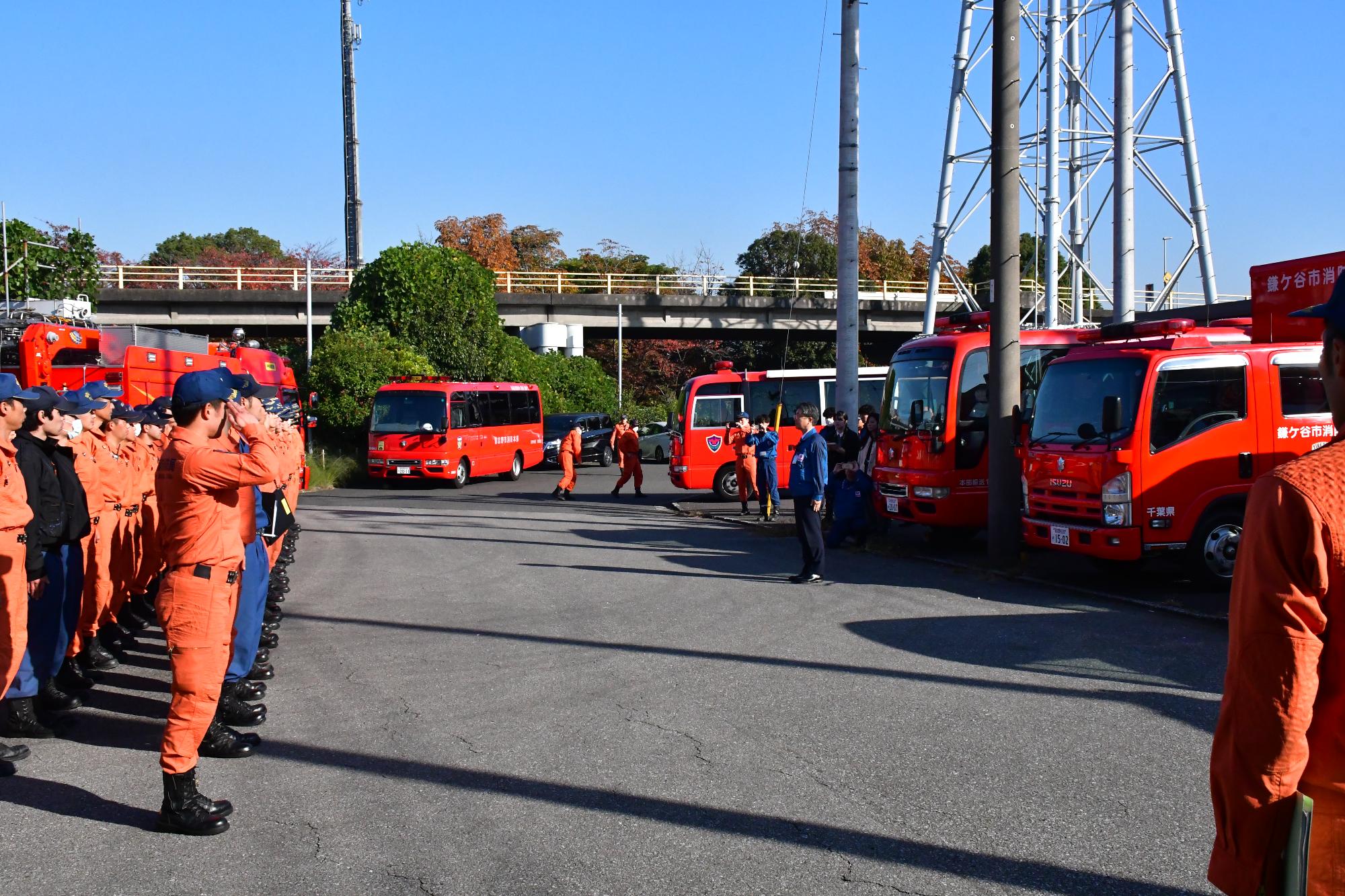 青空の下、訓練開始にあたり、開会式が行われている様子で、消防職員50名がきれいに整列し、東京電力パワーグリッド千葉支社長に対し敬礼をしている様子