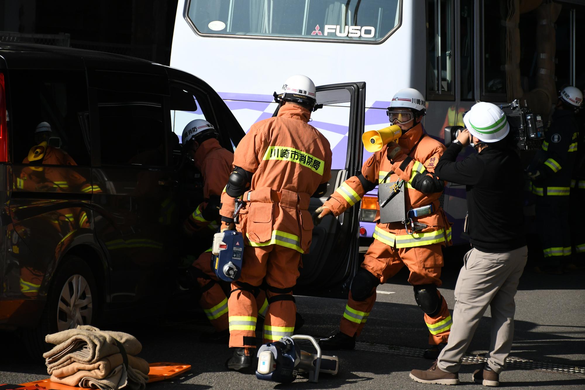 青空の中、救助隊3名が訓練事故車両内に閉じ込められた傷病者を救出するために行動している様子