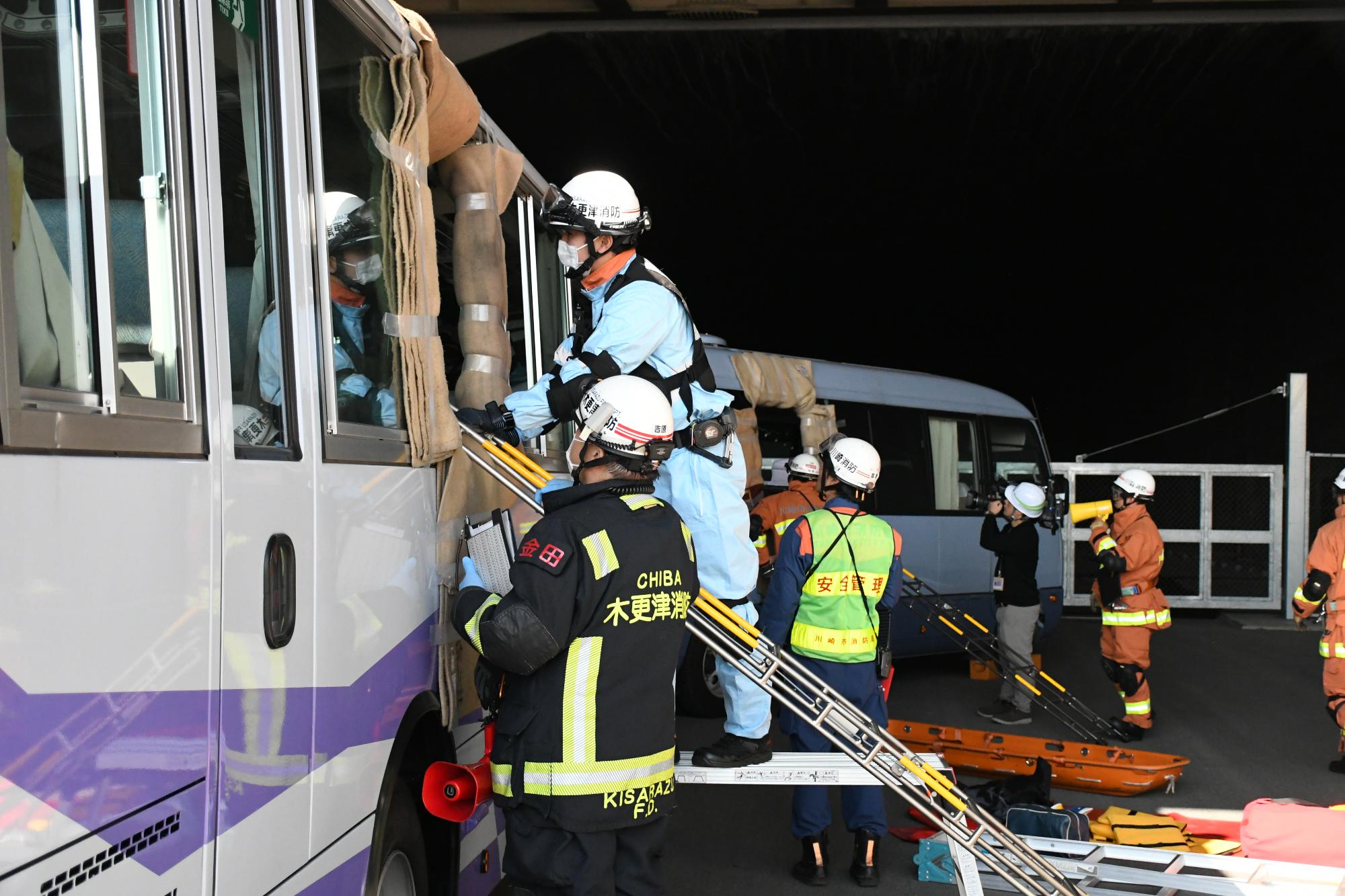 訓練会場であるトンネル内にある訓練事故車両の大型バスにおいて、大型バス内にいる要救助者を窓から救出するため、消防隊2名がバスの外からバス内で他の救助隊員が救出している様子を確認しながら救出の準備をしている様子。