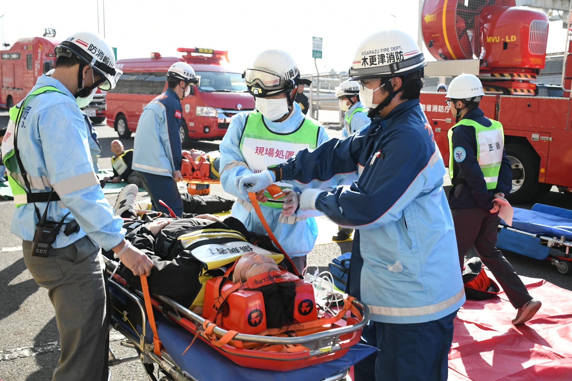 青空の中、大型バスから救出された傷病者を搬送するため、救急隊3名が傷病者をストレッチャーに乗せ搬送の準備をしている様子