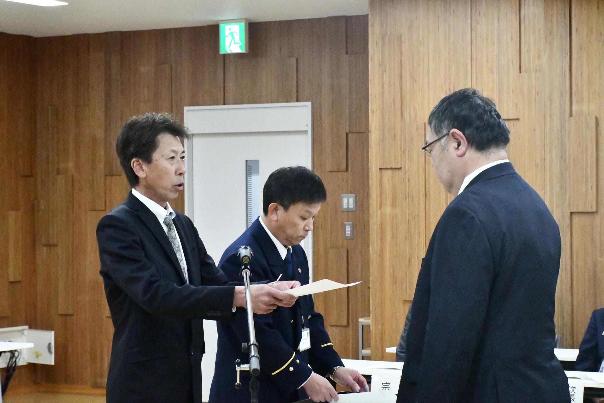 消防団長が消防団の新本部長へ辞令を交付している様子
