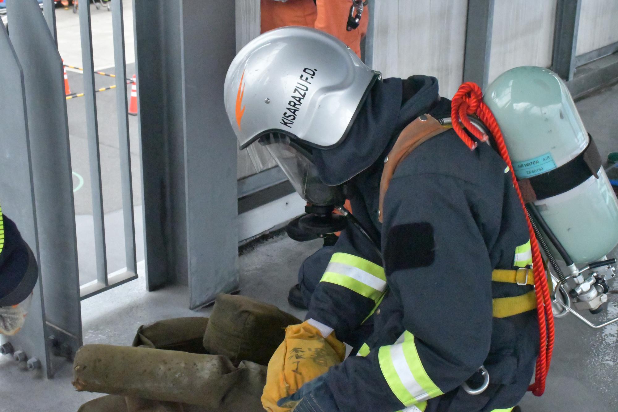 防火衣を着装し空気呼吸器を背負った新規採用消防職員が屋内進入し要救助者を救出しようとしている様子の写真