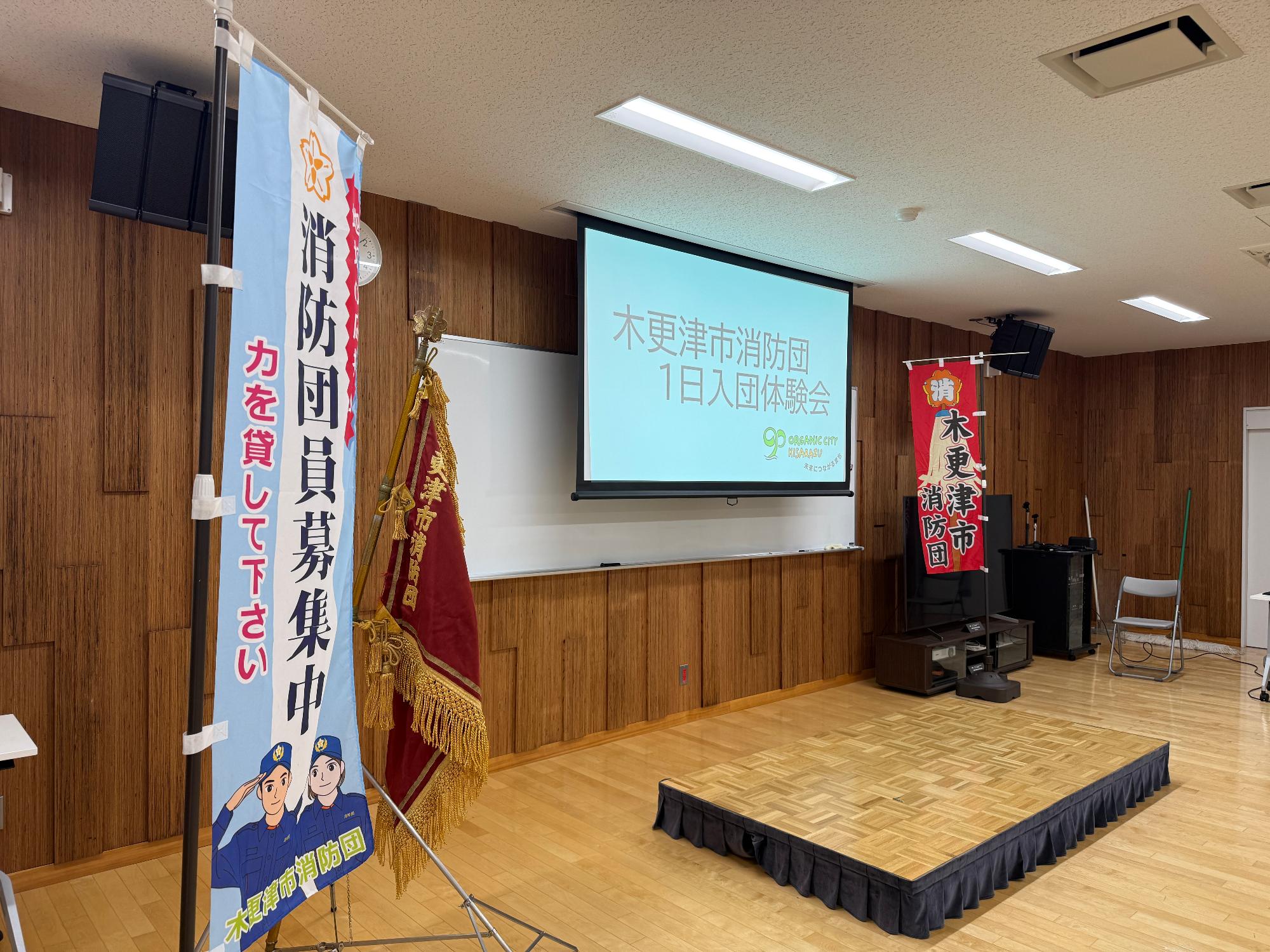 令和8年9月13日に消防本部3階の大会議室内でプロジェクターに映し出された消防団1日入団体験会文字を会議左側から撮影している様子