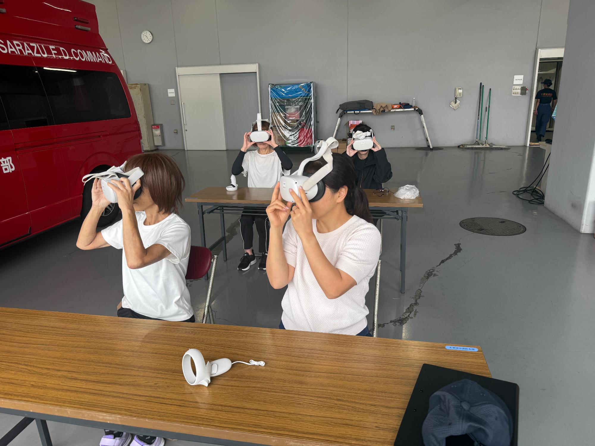 消防本部庁舎の車庫内で、体験会参加者4名がVRを使用して消防車両の緊急走行のVR体験をしている様子