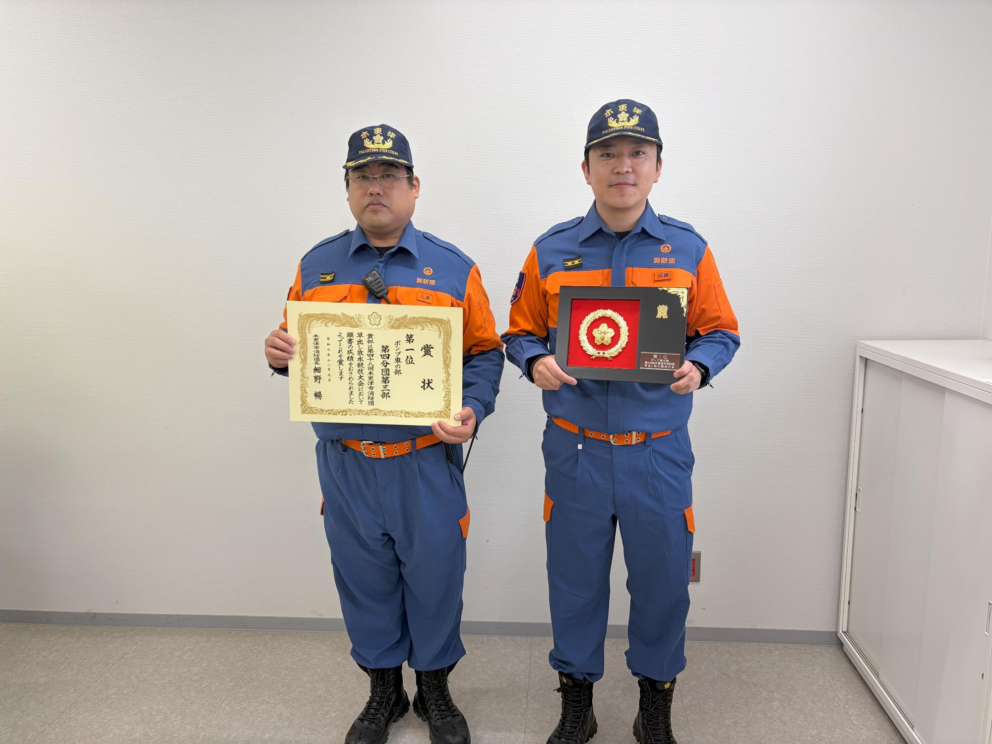消防団員2名が、前列右から1番目の方が盾、右から2番目の方が賞状を持って立っている記念写真