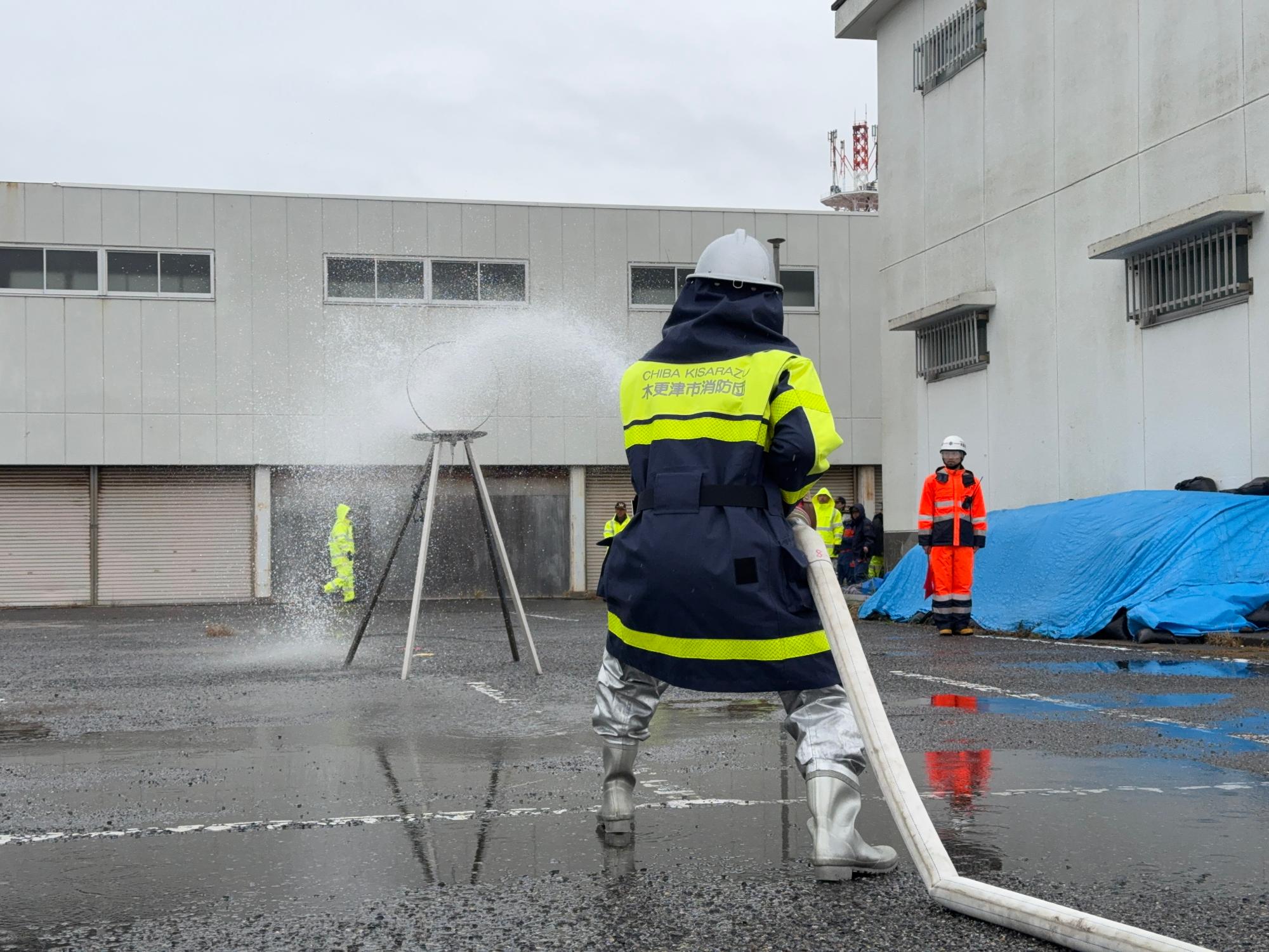 防火服を着た消防団員の方が、両手でホースを抱え「火」と書かれた的に向けて放水をしている写真
