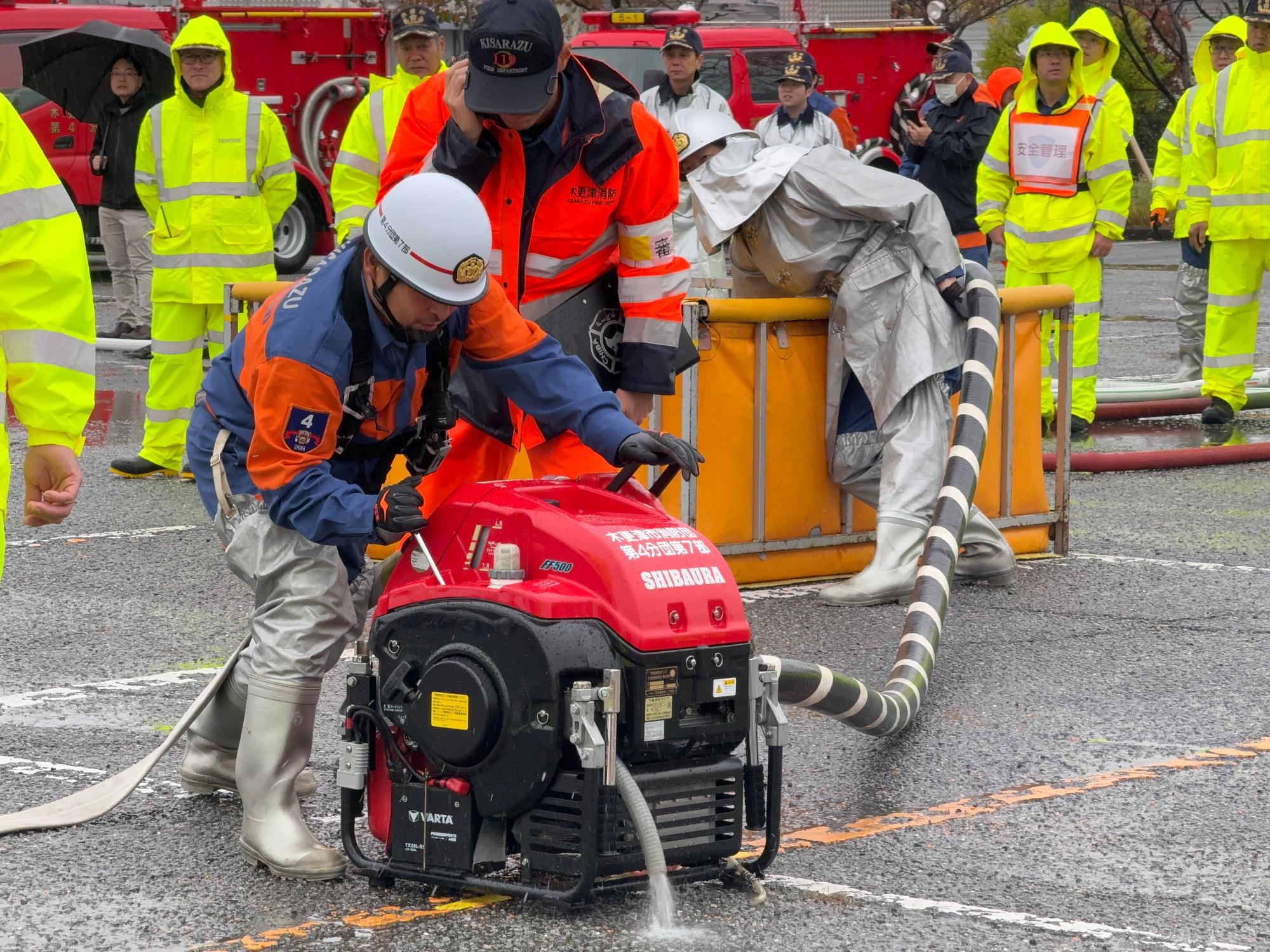 ヘルメットを着用した消防団員が小型動力ポンプを操作している様子の写真