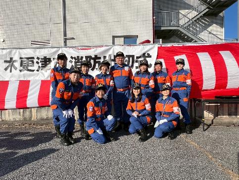 青空の下木更津市消防出初式の垂れ幕と紅白幕をバックに当時の消防団長と機能別分団女性部10名の集合写真