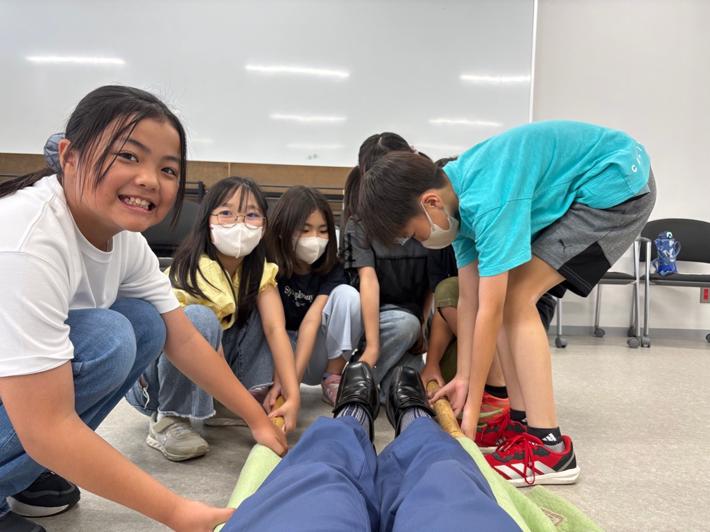 子供たちが毛布と竹で作成した担架を使って大人を持ち上げている様子