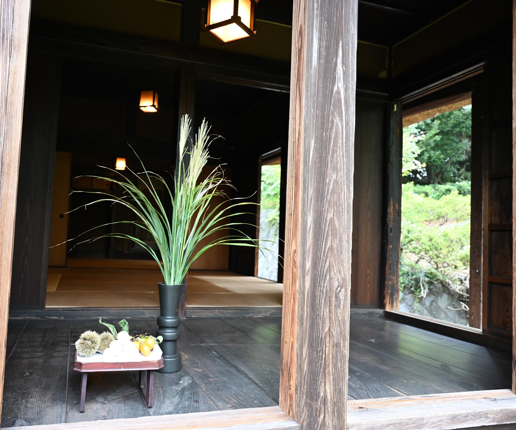 木造家屋の旧安西家住宅に、ススキ、団子、栗、柿が十五夜の飾りつけとして展示されている写真です。