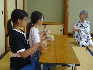 子どもたちが、お茶のいただき方を先生から教わりながら練習している様子