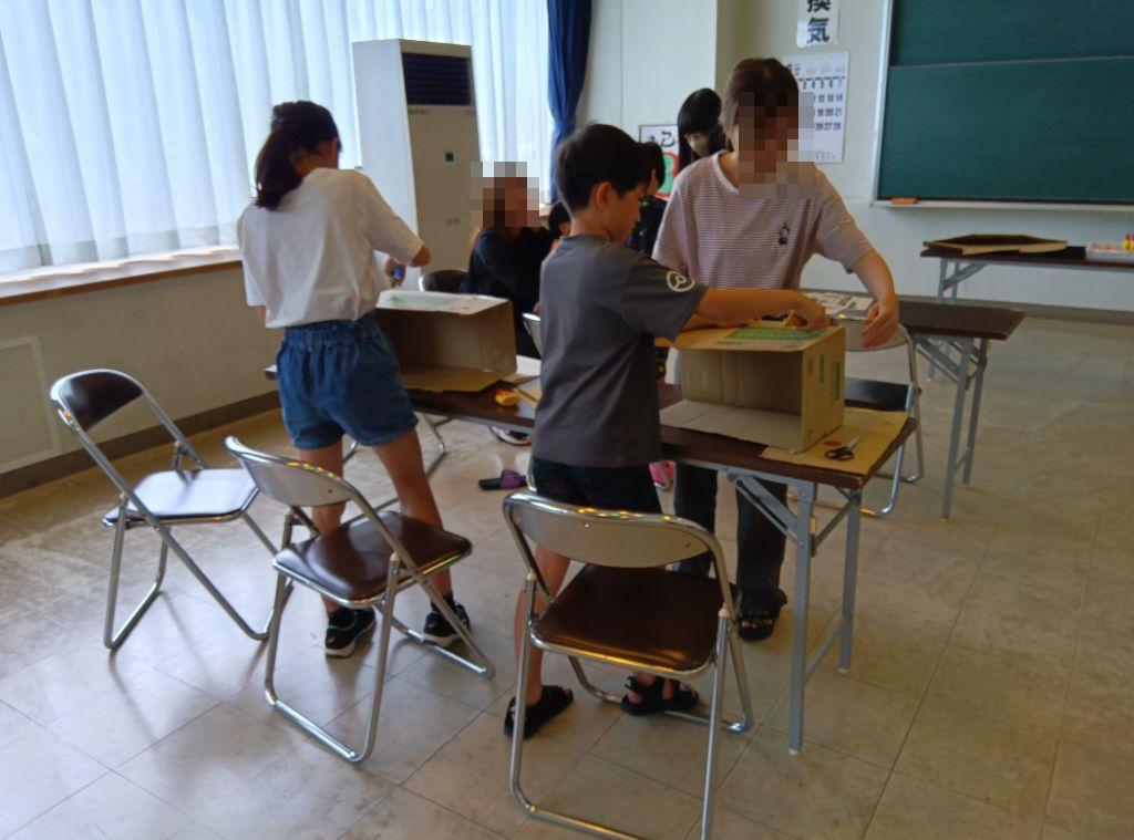 小学生の男女が保護者の力を借りながらソーラークッカーを作っている様子