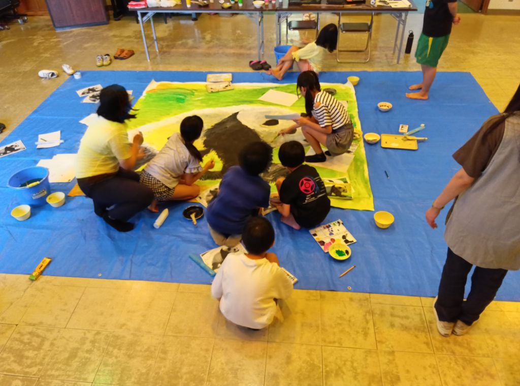 小学生の男女が8畳ほどのブルーシートの上で等身大のパンダを描く様子